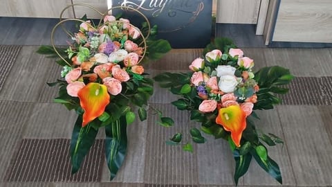 Two pastel flower arrangements with pink roses, orange calla lilies, and green foliage displayed on a striped floor