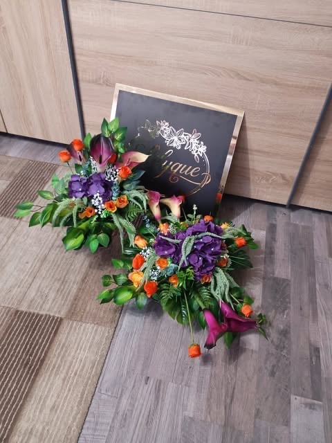 Colorful floral arrangement with orange, purple, and pink flowers on wooden floor next to a chalkboard sign
