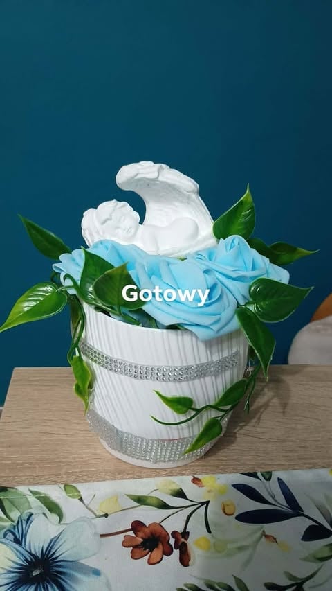 Decorative floral arrangement with white and blue roses in a white ribbed vase with green leaves and silver accents on wooden surface