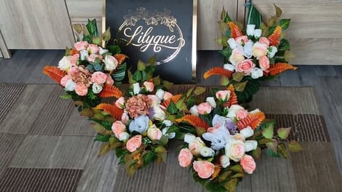 Three floral arrangements with pink roses, white flowers, and greenery flanking a black Lyrique sign on wooden flooring