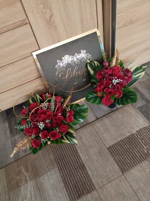 Two burgundy floral arrangements with red roses and greenery beside a black chalkboard sign on wooden floor