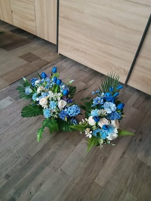 Two blue and white floral arrangements with greenery displayed on a dark wooden floor next to light wood cabinets