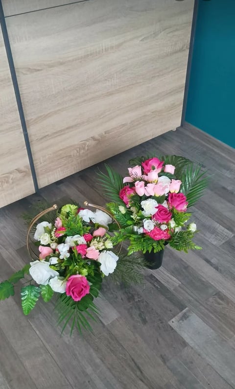Two flower arrangements with pink and white roses on dark wood floor against teal wall and light wood cabinet