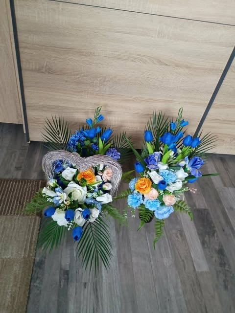 Two decorative floral arrangements with blue iris flowers, roses, and greenery displayed on dark flooring indoors