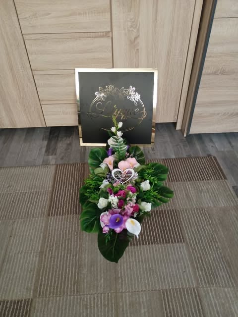 Floral arrangement with white and purple flowers displayed below a black chalkboard with gold-leaf flower design on tiled floor