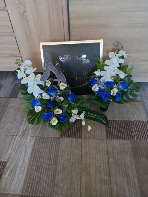 Floral display with white and blue flowers arranged around a chalkboard sign on wooden flooring