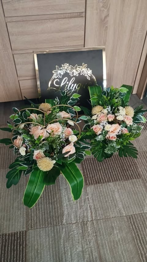 Floral arrangement with peach roses, white gerberas, and green foliage displayed in front of a chalkboard sign against wooden wall paneling.