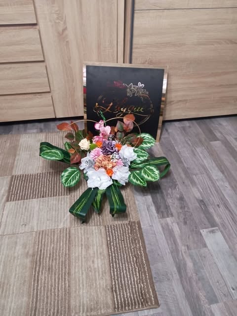 Colorful flower bouquet with white, pink, and orange blooms tied with green ribbon, displayed on wooden flooring next to a black gift box