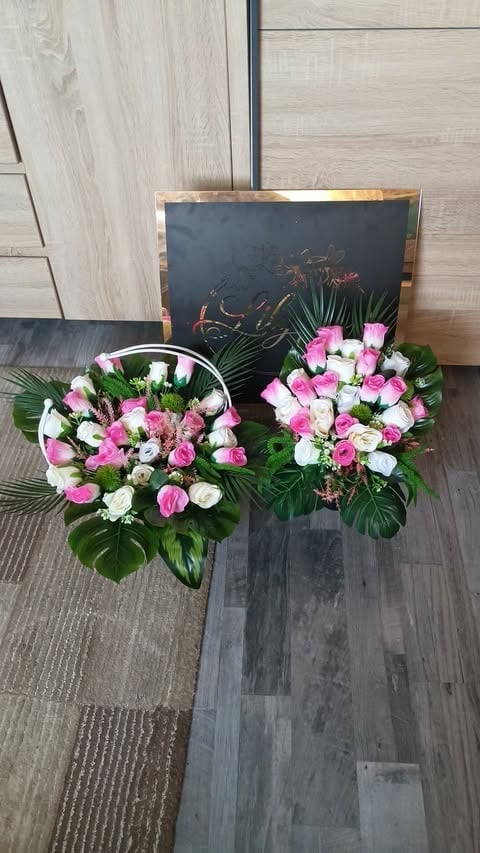Two pink and white floral arrangements in baskets displayed on wooden flooring with a dark board in the background
