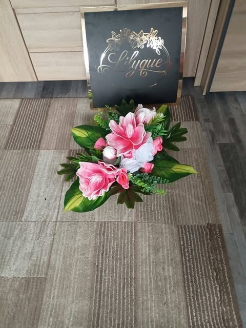 Elegant storefront display with black sign reading Oblique in gold script lettering, decorated with pink and white flowers and green foliage on wood flooring.