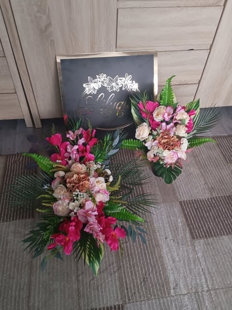 Three vibrant wedding bouquets with pink, magenta, and cream flowers, green foliage, displayed on gray flooring with a chalkboard sign
