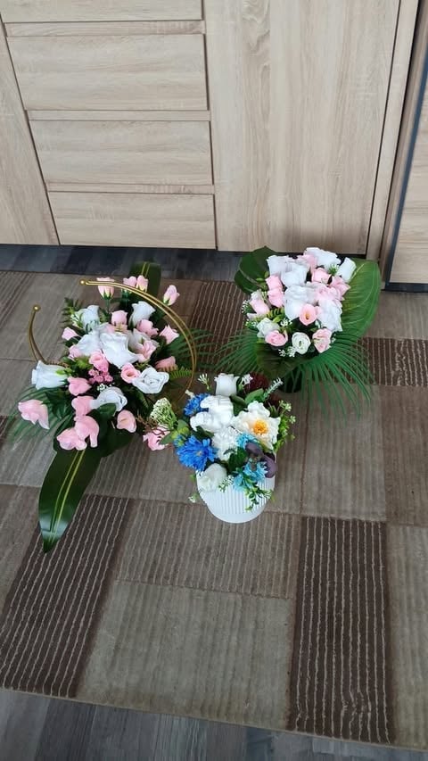 Three floral arrangements with pink, white, and blue flowers in vases on a striped gray floor against light wood cabinetry