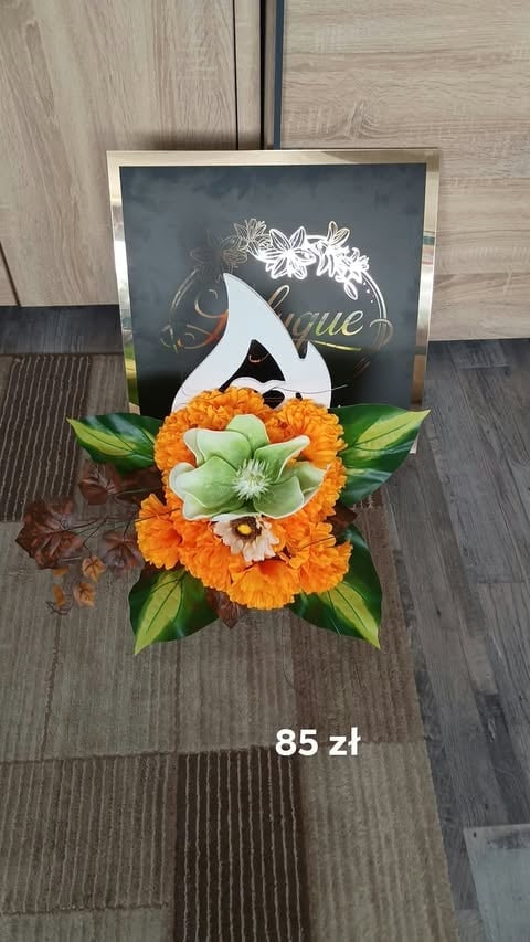 Decorative floral greeting card with orange gerbera daisies and green leaves on dark background, priced at 85 zł