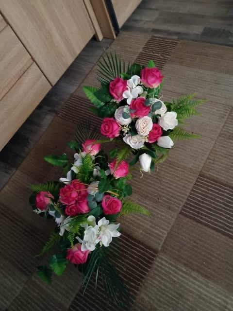Long floral arrangement with pink roses, white flowers, and green foliage on a striped indoor floor