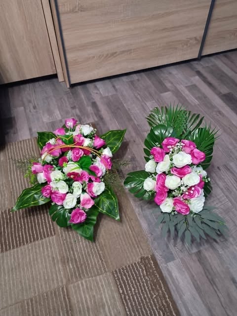 Two funeral flower arrangements with pink and white roses on a gray wood floor against light wooden cabinet doors.