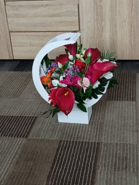 Red and pink flowers arranged in a white curved box on a striped gray floor with wooden wall background