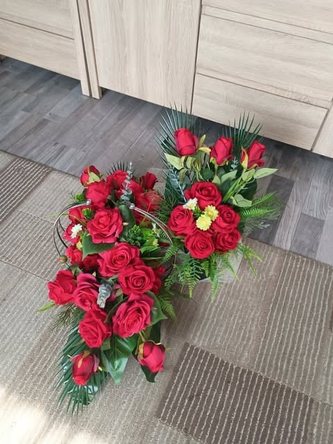 Red rose casket spray floral arrangement with pink roses and white flowers on gray tile floor near light wood doors