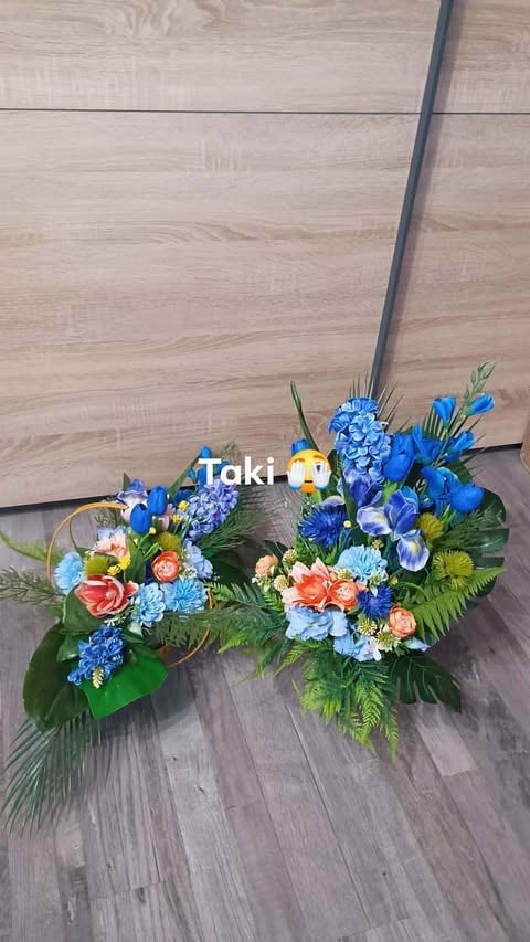 Colorful flower arrangement with blue hydrangeas, delphiniums, and peach roses on wooden floor next to gray metal pole
