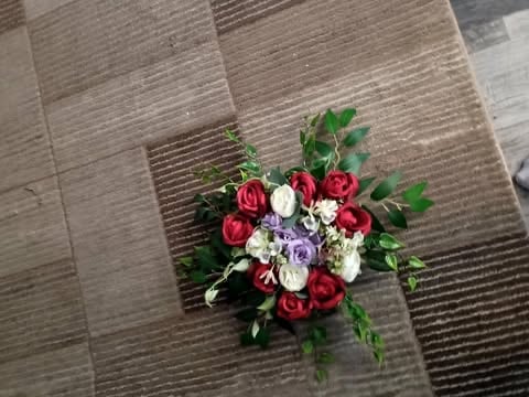 Overhead view of a vibrant bridal bouquet with red roses, white flowers, and purple blooms on a textured wooden floor
