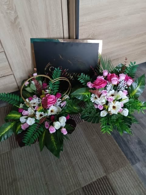 Two floral arrangements with pink, white, and deep red flowers with green foliage and a black sign board behind them on a wooden floor.