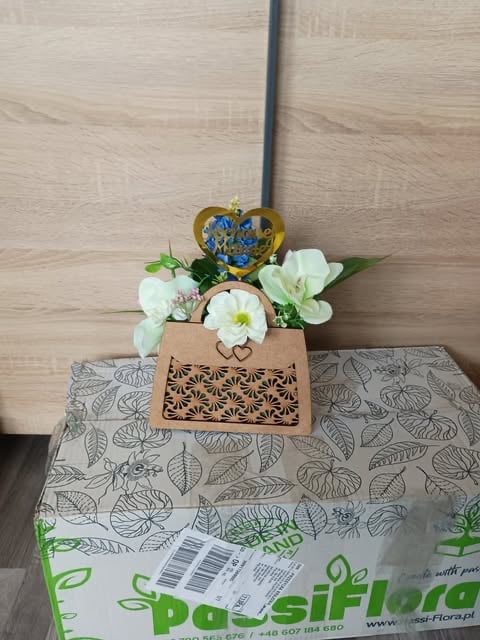 Potted white flowers with golden heart ornament in tan ceramic planter on branded gift box with wooden floor background
