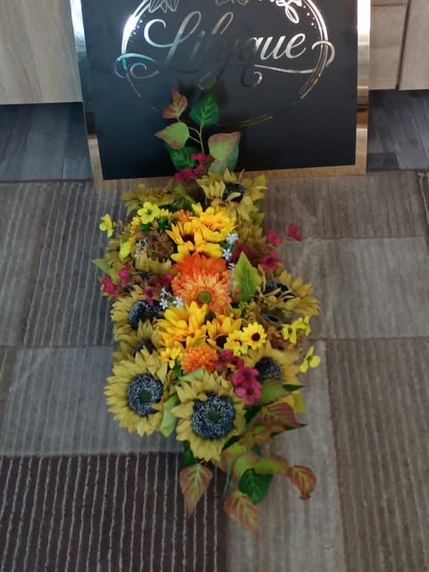 Colorful flower arrangement with sunflowers, gerbera daisies, and purple flowers displayed on gray flooring beneath a dark sign