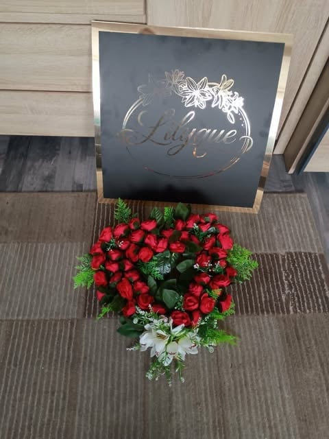 Red rose arrangement with greenery displayed beneath a Welcome sign on a wooden easel