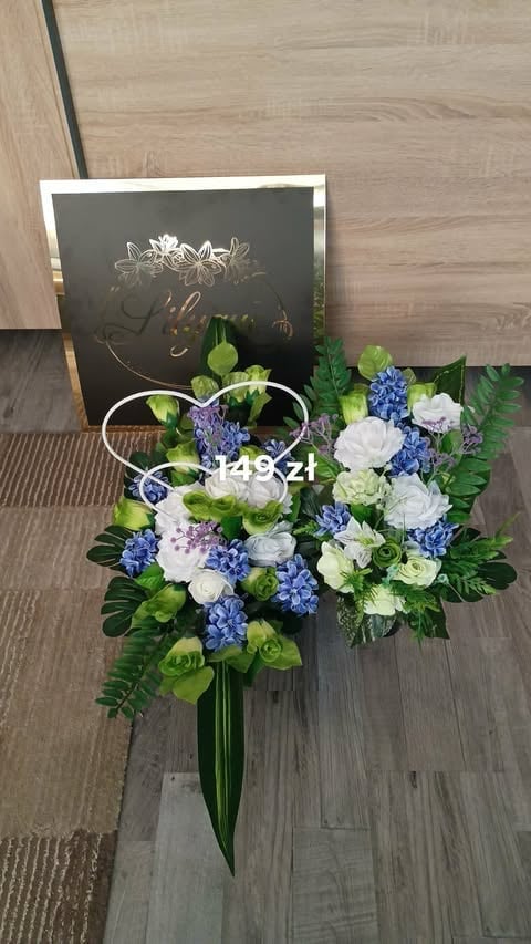 Floral arrangement with white roses, blue hydrangeas, green cymbidiums, and ferns in a white handle display on wooden floor with chalkboard backdrop