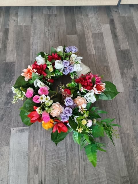 Vibrant floral arrangement with red, pink, purple, and white flowers with green foliage on wooden floor
