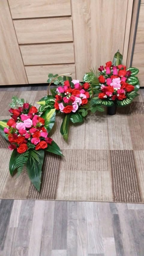 Three red and pink floral arrangements with green foliage displayed on wooden flooring indoors