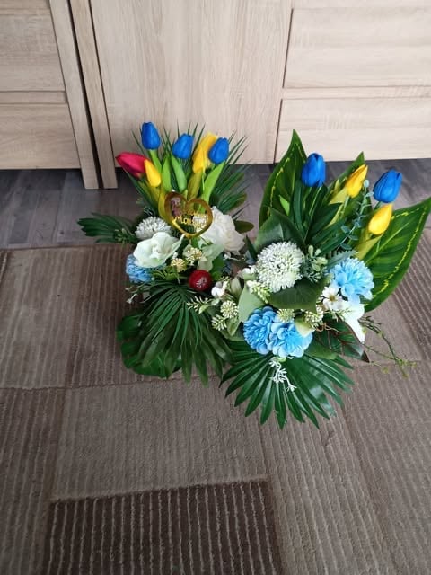 Colorful floral arrangement with blue, yellow, and pink tulips, white and blue carnations, and green foliage on an indoor floor