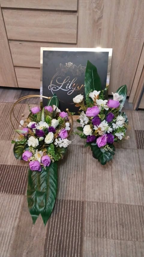Two floral arrangements with purple and white flowers next to a chalkboard sign reading Lily on wooden flooring