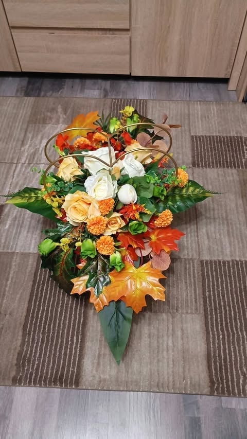 Autumn floral arrangement with white roses, orange carnations, red flowers, and fall foliage on wooden floor