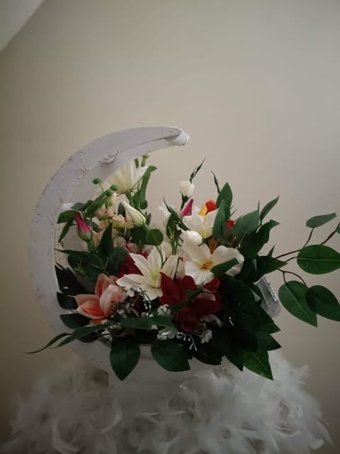Crescent-shaped moon vase holding a floral arrangement with white and red flowers, green foliage, and white tulle netting base