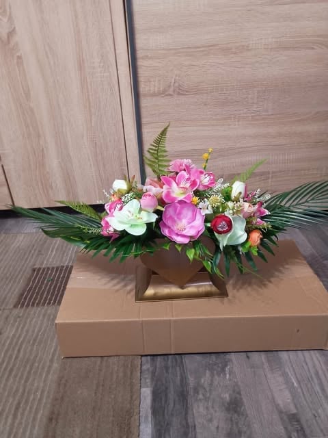 Pink and white flower arrangement in bronze square vase on cardboard box against wood paneling