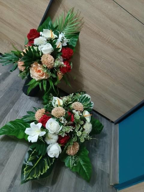 Two cascading floral arrangements with red roses, white flowers, peach dahlias, and tropical green foliage on wooden flooring