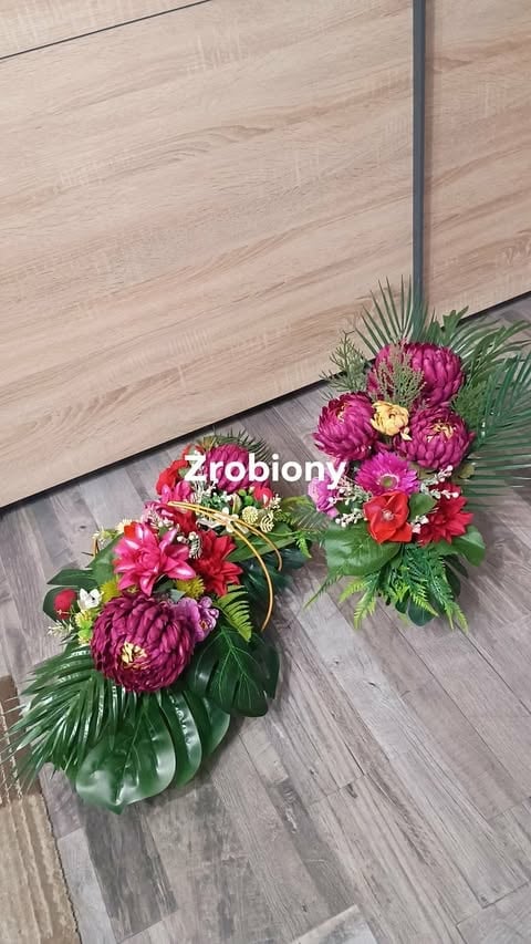 Two vibrant floral arrangements with magenta peonies, red flowers, and green foliage on a wood floor against a light wooden wall