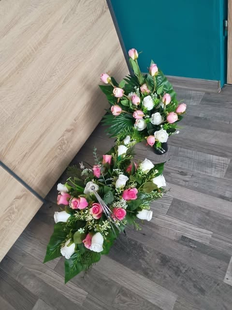 Tiered floral arrangement with pink and white roses and carnations on gray wood flooring next to teal furniture