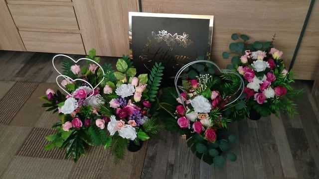 Three floral arrangements with pink, white, and purple flowers in wicker baskets on a wooden floor near a blackboard