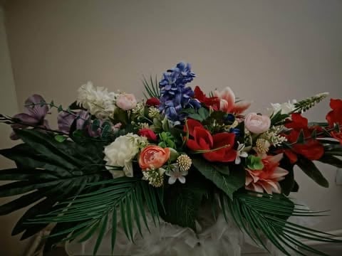 Colorful flower arrangement with blue hyacinths, red carnations, pink roses, and green palm fronds in a horizontal table centerpiece