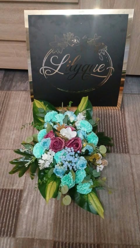 Elegant black sign with Liane script logo displaying a vibrant floral arrangement with turquoise, pink, and white flowers with green foliage