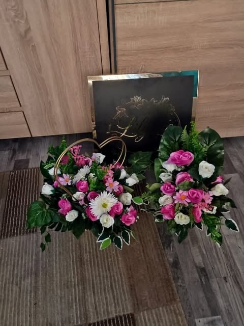 Floral arrangement with pink roses and white flowers in front of a black gift box, displayed on wooden flooring
