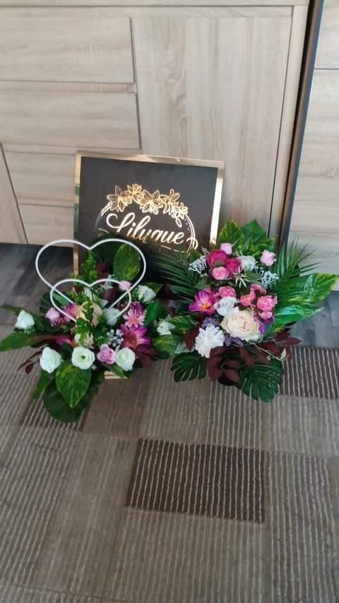 Two floral arrangements with pink and white flowers next to a black sign with gold text reading Lilmue