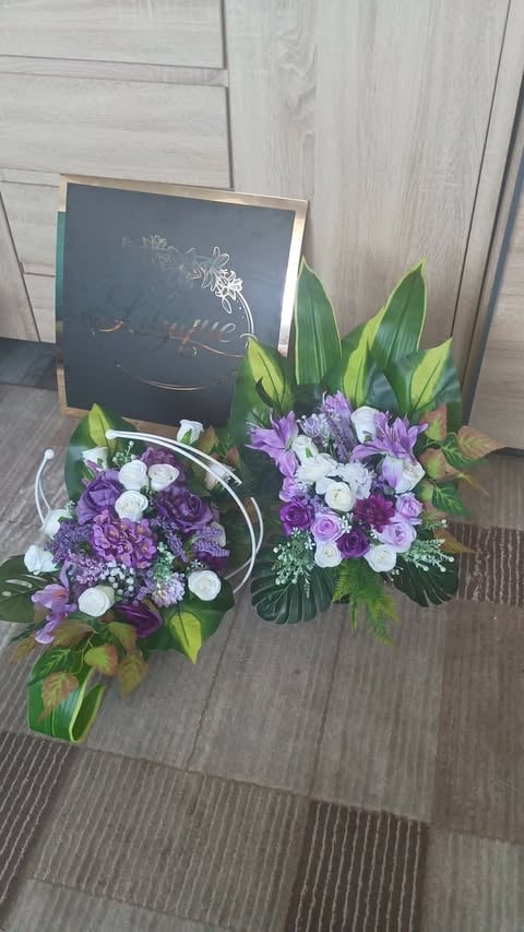 Two floral arrangements with purple and white flowers, green foliage, and a dark chalkboard sign displayed on wooden flooring