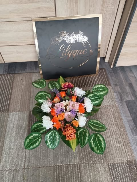 Colorful flower bouquet with white, orange, pink, and purple blooms arranged on a dark chalkboard sign reading Clique