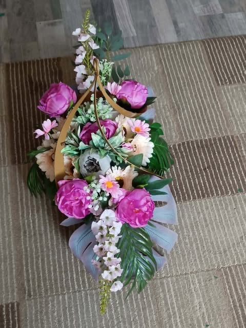 Floral arrangement with pink peonies, white flowers, and green foliage tied with blue and gold ribbons on textured flooring