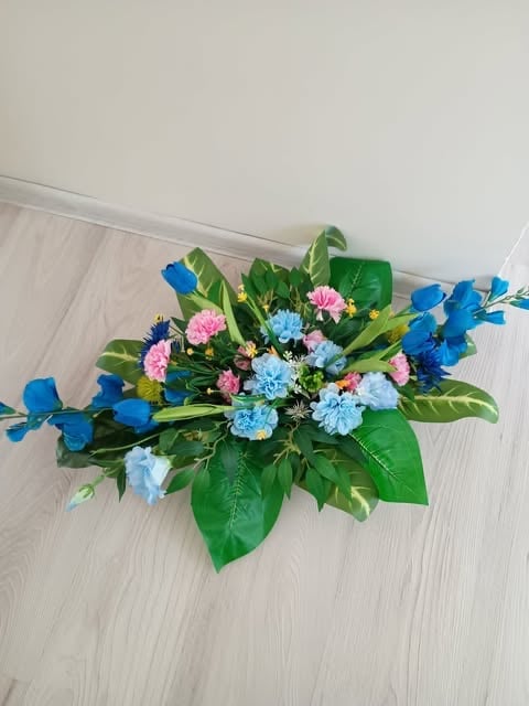 Colorful floral arrangement with pink and blue carnations, blue iris stems, and green foliage on a light wooden floor