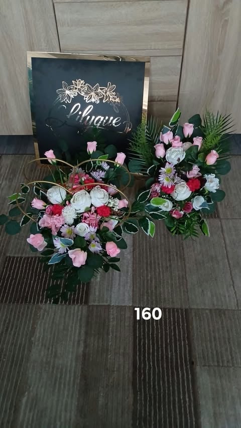Two floral arrangements with pink and white flowers displayed in front of a chalkboard sign on wood flooring