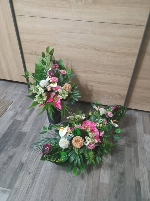 Two floral arrangements with pink, white, and burgundy flowers arranged in black vases on gray flooring against wooden wall paneling