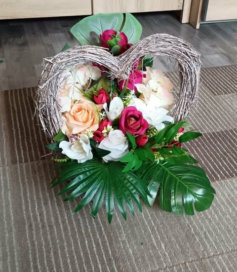 Heart-shaped floral arrangement with mixed flowers including roses, orchids, and tropical leaves in white, pink, and red tones